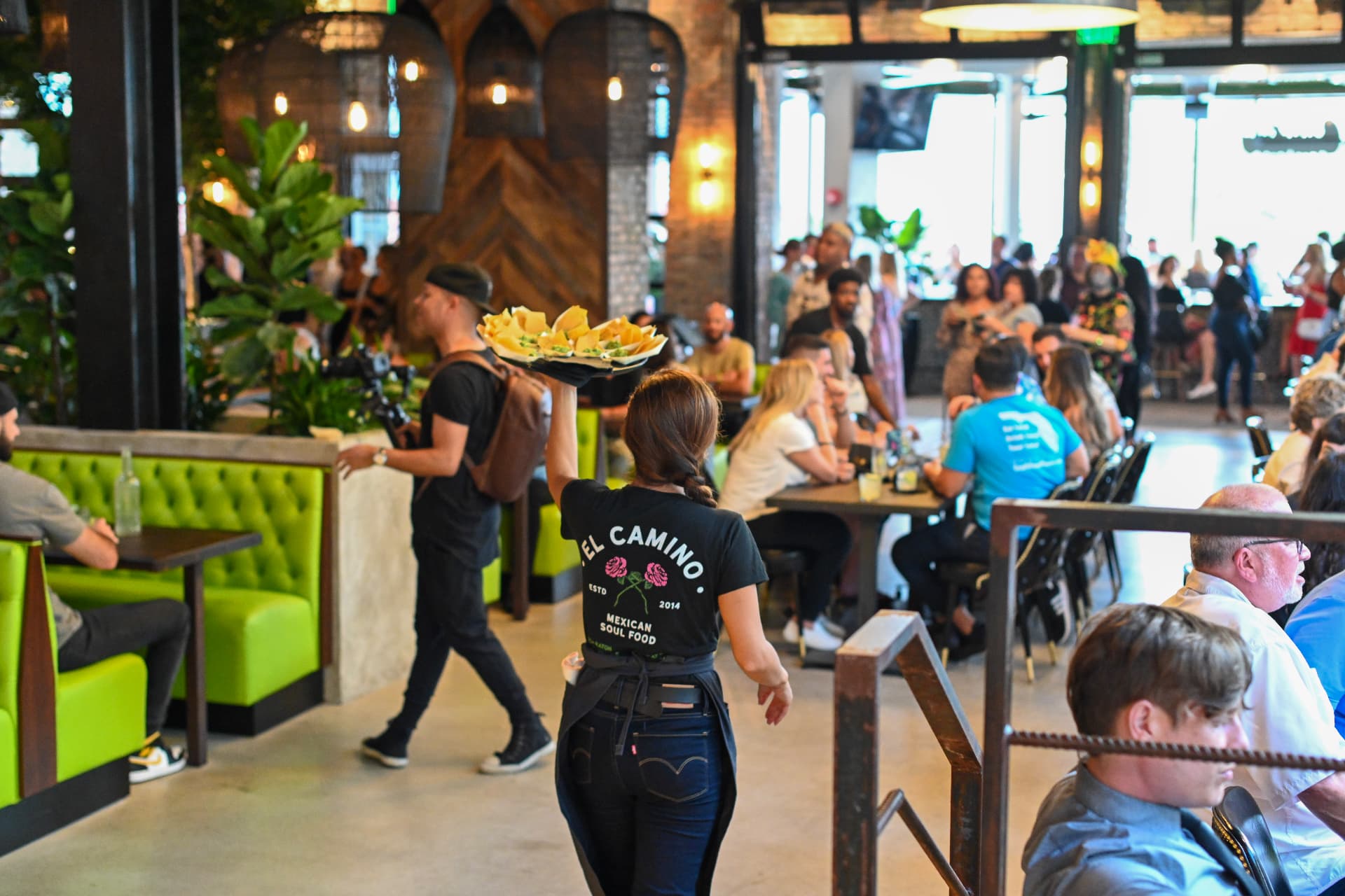 A server carries appetizers through El Camino's dining room, past green booths and guests