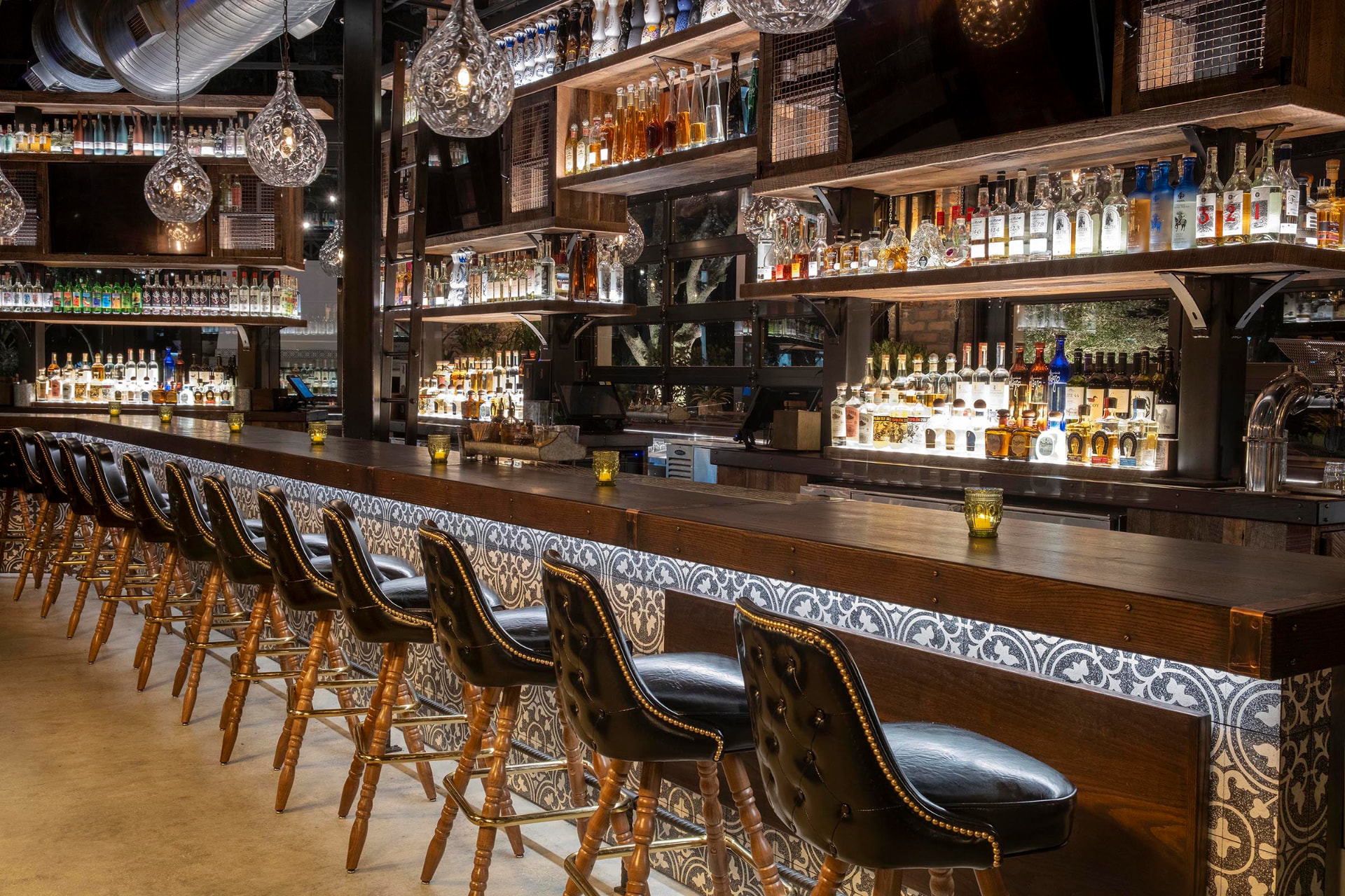 El Camino bar with leather stools, illuminated spirit shelves, and glass pendant lights
